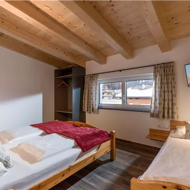 Ein gemütliches Schlafzimmer mit zwei Betten und Holzmöbeln. Große Fenster bieten einen Blick auf die winterliche Landschaft.