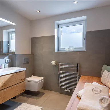 Ein modernes Badezimmer mit Holzschränken und einer Fensterlichtquelle. Die Wände sind in sanften Grautönen gehalten.