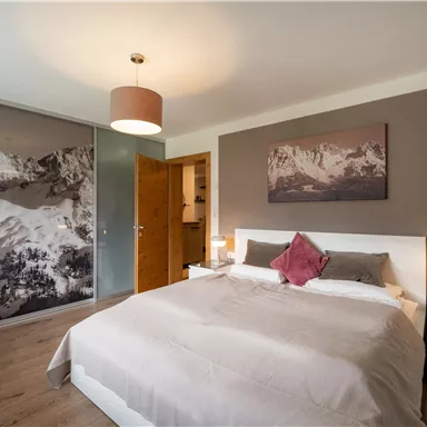 Ein modernes Schlafzimmer mit einem großen Bett und einem gemütlichen Ambiente. Ein Bild der Berge ist an der Wand, und es gibt einen Kleiderschrank aus Glas.