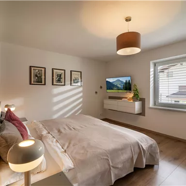 Ein modernes Schlafzimmer mit einem Doppelbett und sanfter Beleuchtung. Große Fenster sorgen für Tageslicht und eine angenehme Atmosphäre.