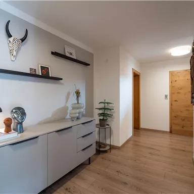 Ein moderner Flur mit einem großen Spiegel und einer stilvollen Kommode. Die Wände sind hell, und es gibt dekorative Elemente sowie einen Holzfußboden.