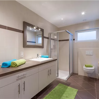 A modern bathroom with a shower, a large mirror, and a sink. Fresh towels in bright colors are placed on the shelf and the floor.