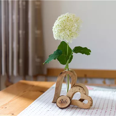 An elegant decoration with a white flower in a vase and heart-shaped wooden figures. The table is made of wood and covered with a red polka-dot table runner.
