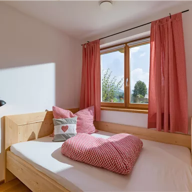 A cozy bedroom with a wooden bed and red curtains. There are heart-patterned pillows on the bed.
