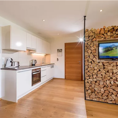 Modern kitchen with elegant white cabinets and wooden details. A television is mounted on the wall next to a sturdy wooden shelf.