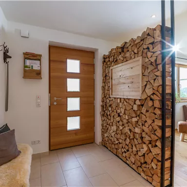 A modern entrance area with wood paneling and a large wood stack wall. The door is made of wood and has several windows.