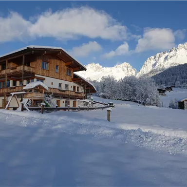 A charming chalet amidst a snowy landscape. In the background, majestic mountains rise under a clear sky.