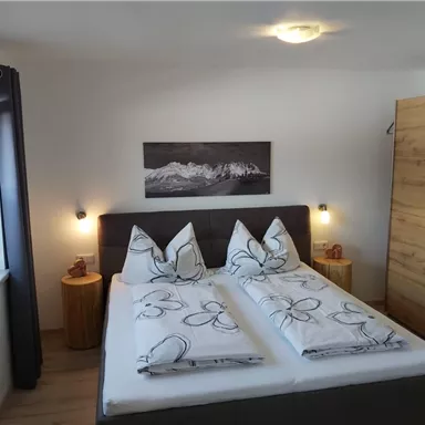 Ein gemütliches Schlafzimmer mit einem großen Doppelbett und dekorativen Kissen. An den Wänden hängen Bilder, und das Zimmer hat eine helle, einladende Atmosphäre.