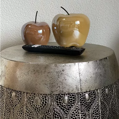Two decorative glass apples are sitting on a table. Next to them, a remote control is resting on the tabletop.