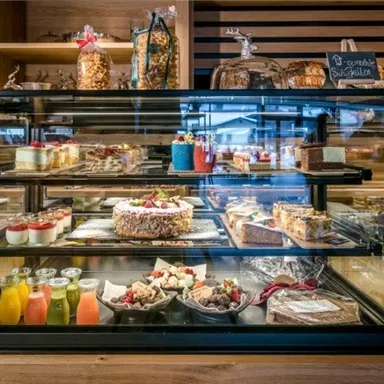 A counter with various desserts and pastries in a modern setting. Cakes, puddings, and fruity drinks are beautifully displayed on the shelves.