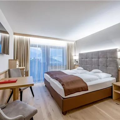 Ein modernes Hotelzimmer mit einem Doppelbett und eleganter Einrichtung. Große Fenster sorgen für viel Tageslicht und einen Blick nach draußen.