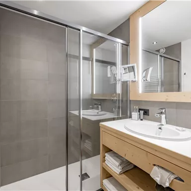 Ein modernes Badezimmer mit einer Dusche aus Glas und einem großen Spiegel. Die Möbel sind aus hellem Holz und die Wände sind in neutralen Farben gehalten.