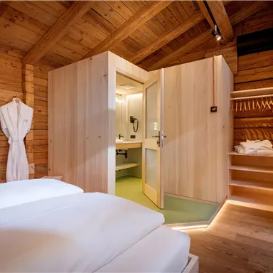 A cozy room with a wooden ceiling and two beds. In the background, a bathroom with modern elements can be seen.