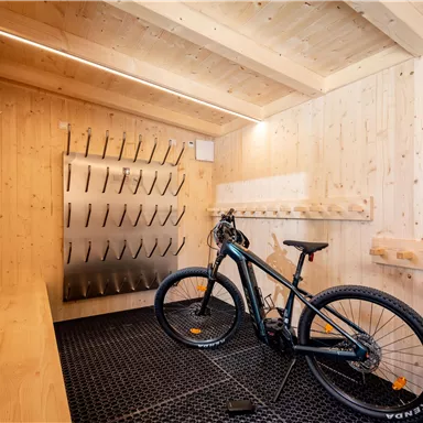 A modern bicycle room with wooden paneling. A bicycle is on the floor, while there are hanging options available on the wall.