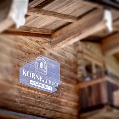 A wooden chalet with a sign that reads "KORNKammer Apartments." The facade radiates coziness and an alpine atmosphere.