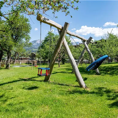 A beautiful playground with two swings in a green meadow. In the background, trees are growing under a blue sky.