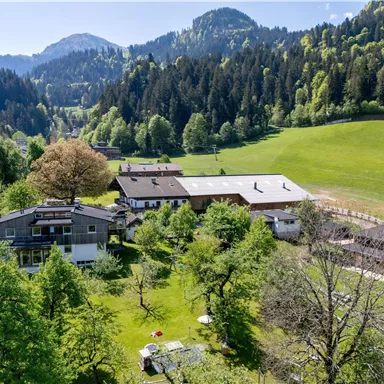 A picturesque landscape with green areas and mountains in the background. In the foreground, several houses and trees can be seen.