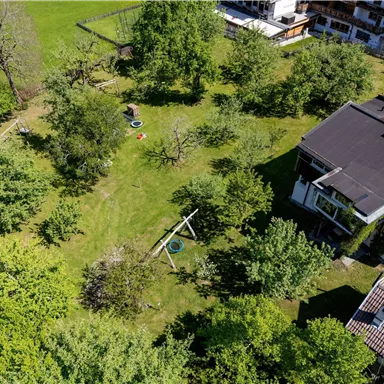 A green meadow with many trees and houses in the background. It is a sunny day and the landscape looks inviting.