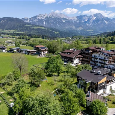A picturesque landscape with green meadows and mountains in the background. The houses are nestled in a rural setting.