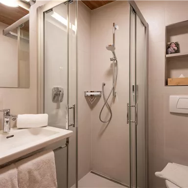 A modern bathroom with a shower and a sink. There are bright walls and some towels as well as toiletries on a shelf.
