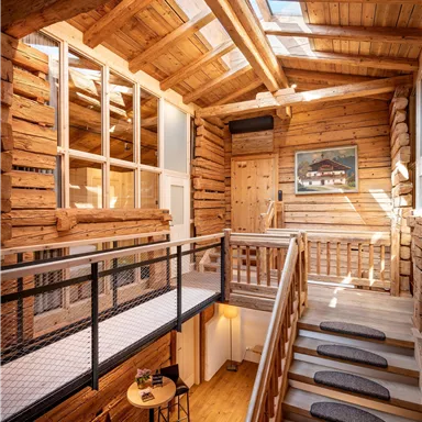 A cozy wooden staircase leads to a modern room with wood paneling and large windows. The room has a warm, inviting ambiance.