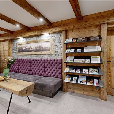 A cozy reception area with a purple sofa and a wooden table. A bookcase with informational materials stands against the wall.