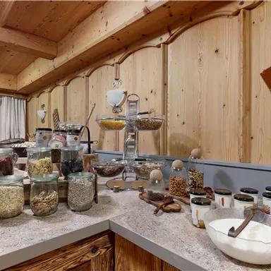 A cozy kitchen with wooden walls that displays a wide selection of storage jars and food. Various ingredients and a note can be seen on the counter.