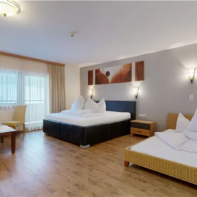 A modern hotel room with two beds and a cozy armchair. Large windows provide plenty of daylight.