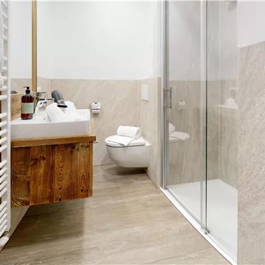 A modern bathroom with a shower and a wooden shelf. The walls are designed with bright tiles and a wood look.