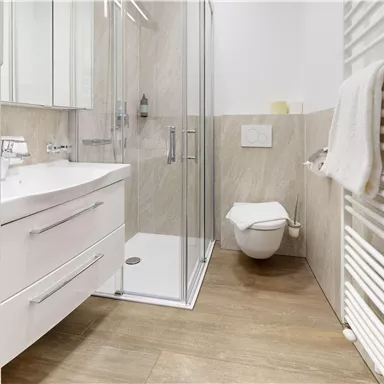 A modern bathroom with a shower cubicle and white bathroom furniture. The floor is made of wood and there is a towel holder on the wall.