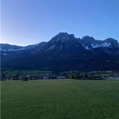 Eine wunderschöne Berglandschaft mit schneebedeckten Gipfeln und grünen Wiesen. Der klare Himmel bietet einen perfekten Blick auf die Natur.