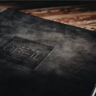 Ein schwarzes Notizbuch mit einem geprägten Logo. Die Oberfläche hat eine elegante, matte Textur.