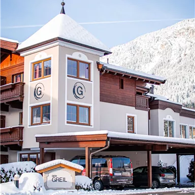 Ein modernes Gebäude mit einem Turm in einer schneebedeckten Landschaft. Es gibt mehrere Autos unter einem überdachten Parkplatz.