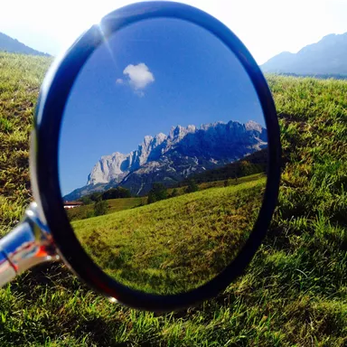 A mirror shows the reflected mountain landscape with green grass and a blue sky. The view is clear and impressive.