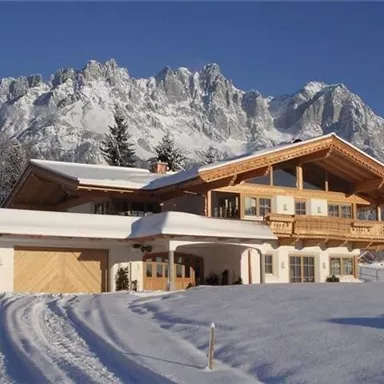 Ein schönes, modernes Chalet im Schnee, umgeben von majestätischen Bergen. Die ruhige Winterlandschaft strahlt Gemütlichkeit aus.