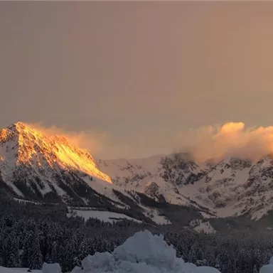 An impressive mountain landscape at sunset. The snow-covered peaks glow golden in the warm light.