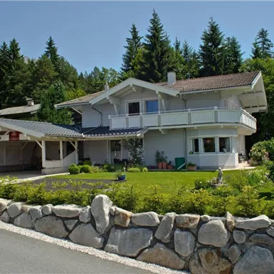 Ein modernes Haus mit Balkon und umlaufendem Garten. Umgeben von Bäumen und einer steinernen Auffahrt.