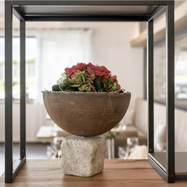 Eine elegante Vase mit bunten Blumen steht in einem modernen Rahmen. Der Hintergrund zeigt einen stilvollen Innenraum eines Restaurants.