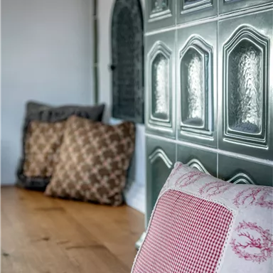 Gemütliche Kissen liegen auf einem Holzboden. Im Hintergrund sind dekorative Fliesen sichtbar.