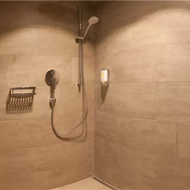 Eine moderne Duschkabine mit fliesenverkleideten Wänden. Es gibt einen Duschkopf und einen praktischen Halter für Duschutensilien.