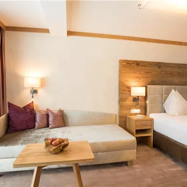 Ein modernes Hotelzimmer mit einem gemütlichen Sofa und einem großen Bett. Das Zimmer ist hell und einladend, mit eleganten Dekorationen.