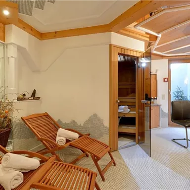Ein entspannender Wellnessbereich mit Holzliegestühlen und einer Sauna. Die Atmosphäre ist ruhig und einladend.