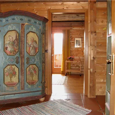 Ein gemütlicher Flur mit einem kunstvoll bemalten Schrank und Holzverkleidung. Im Hintergrund sind weitere Möbel und ein Fenster sichtbar.