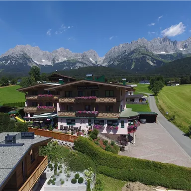 A charming chalet in the Alps with blooming balconies. In the background, majestic mountains rise under a clear blue sky.