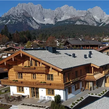 Ein gemütliches Holzhaus mit einem großen Balkon, umgeben von herrlichen Berglandschaften. Die Sonne scheint über die malerische Umgebung.