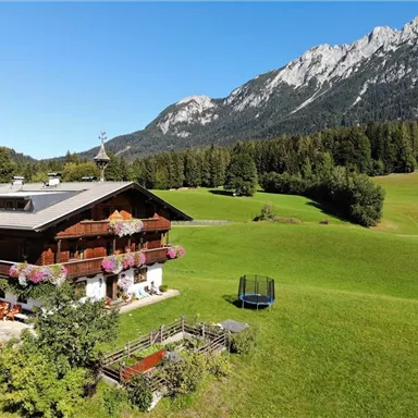 Ein charmantes Landhaus umgeben von grünen Wiesen und Bergen. Der Garten ist mit Blumen geschmückt und bietet eine Ruhezone mit einer Trampolin.