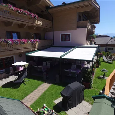 A cozy garden with sun umbrellas and comfortable seating. The adjacent buildings have beautiful balconies adorned with flowers.