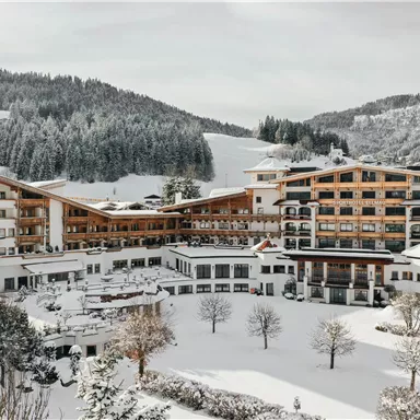 A picturesque hotel nestled in a snowy landscape. The surrounding mountains and trees are covered in snow, creating a cozy winter atmosphere.