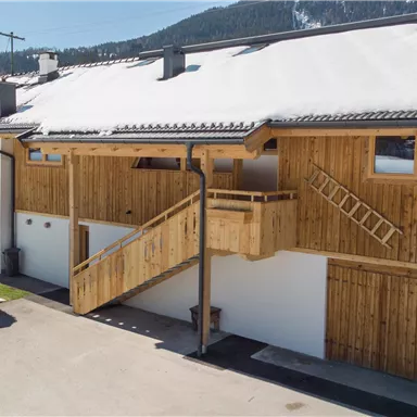 Ein modernes Holzgebäude in einer schneebedeckten Landschaft. Die Struktur hat einen Balkon und eine helle Fassade.
