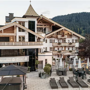 Ein modernes Hotelgebäude in den Bergen mit einem gemütlichen Außenbereich. Es gibt Liegen und Sonnenschirme, um die Umgebung zu genießen.